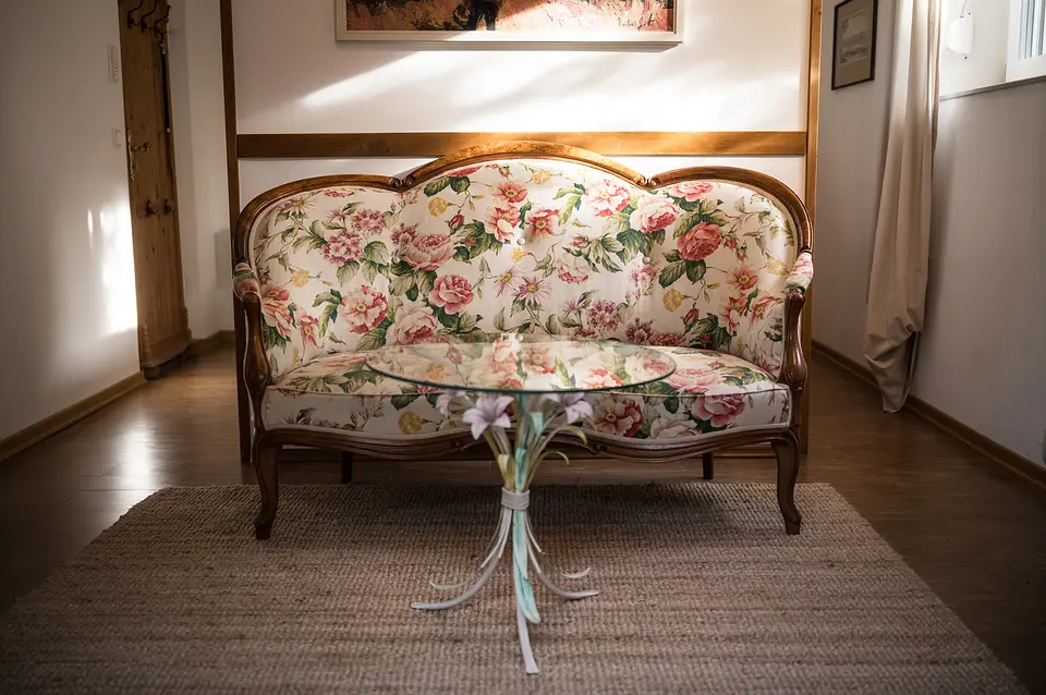 Geblümtes Biedermeier-Sofa mit Glastisch auf Sisalteppich im Gartenzimmer, darüber ein Bild