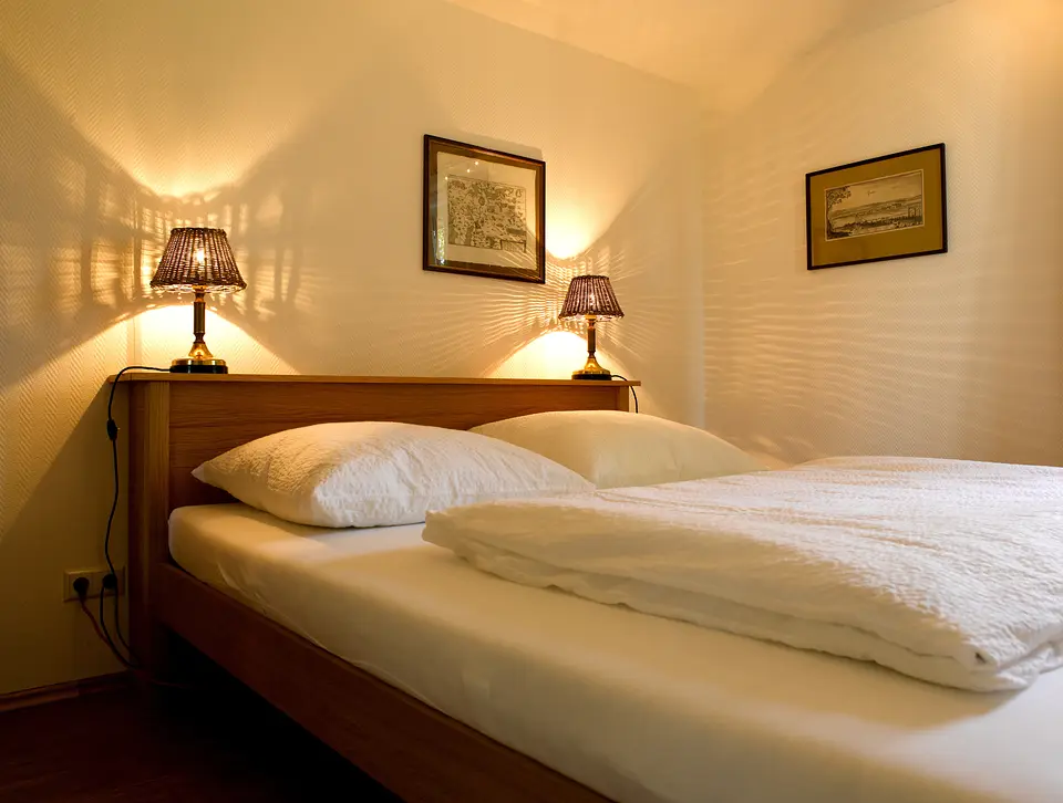Gartenzimmer: Doppelbett aus Holz, zwei Nachttischlampen und alte Stiche an der Wand