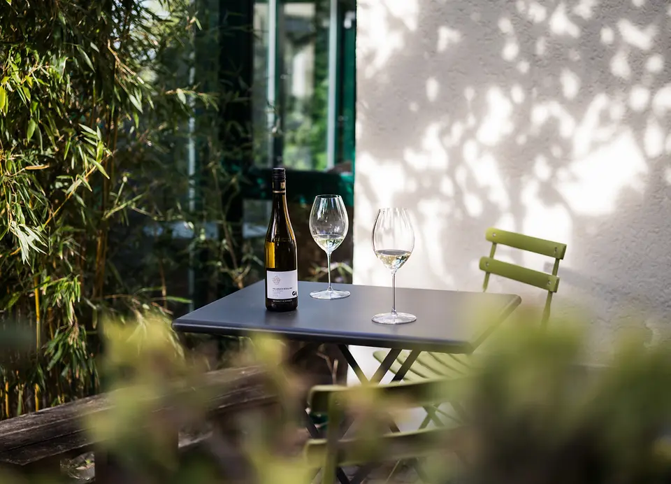 Bistrotisch vor dem Wintergarten des Gartenzimmers mit einer Flasche Wein und zwei Gläsern