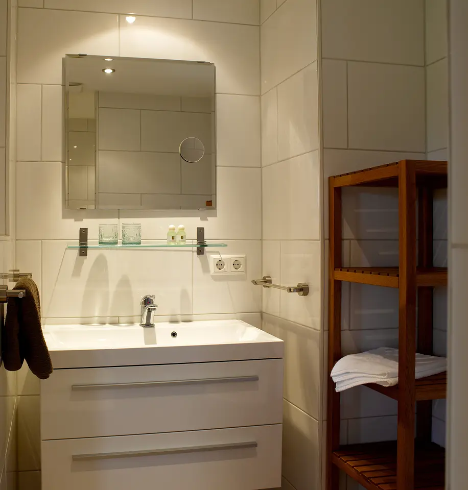 Kleines, elegantes Badezimmer des Gartenzimmers mit Waschtisch, Spiegel und Holzregal mit Handtüchern