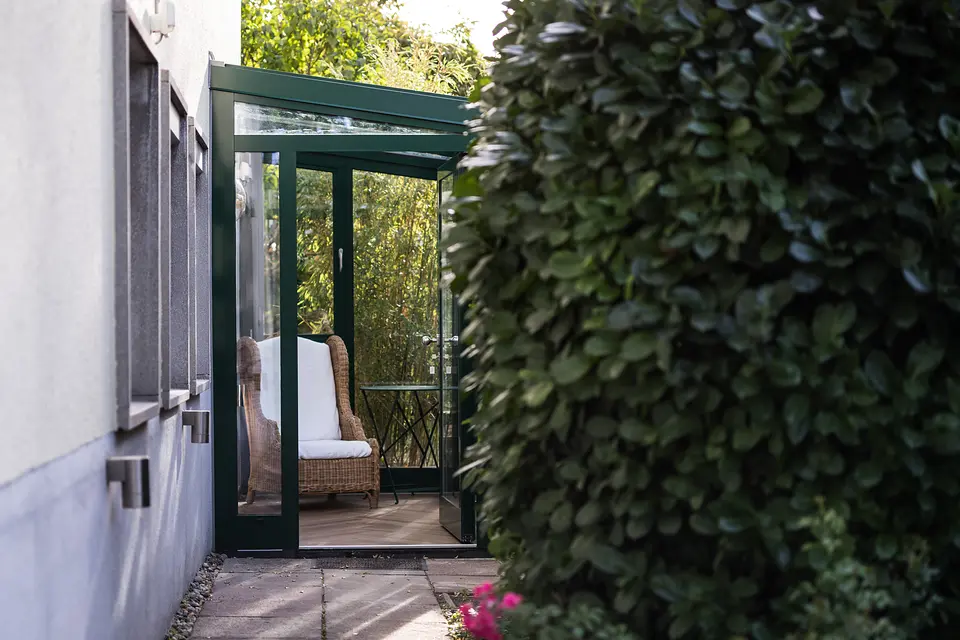 Eingang zum Wintergarten des Gartenzimmers von außen, zwischen Hauswand und Hecke