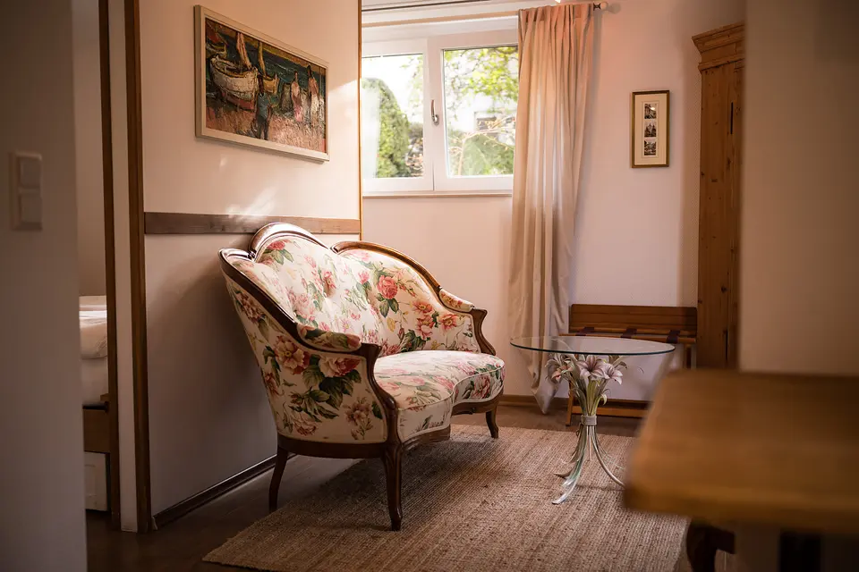 Gartenzimmer: geblümtes Biedermeier-Sofa, Fenster zum Garten, Eckschrank aus Weichholz und Bild mit südlichem Motiv