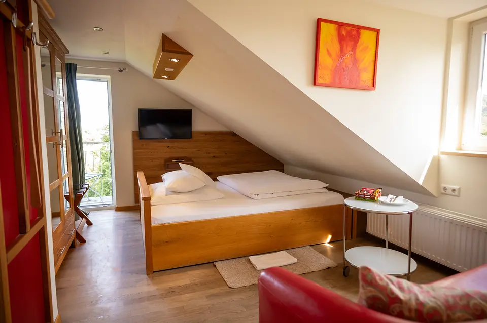 Weinberg-Zimmer unter dem Dach: Doppelbett aus Holz, rote Ledercouch und farbenfrohes Bild an der Dachschräge