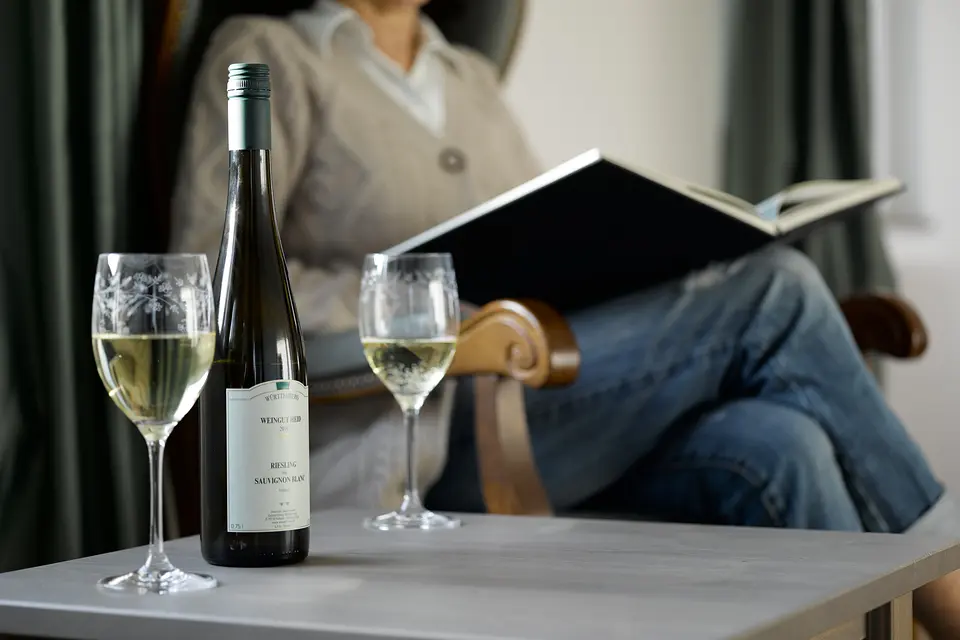 Gast liest im Sessel, auf dem Tisch eine Flasche Fellbacher Riesling und zwei Gläser Weißwein