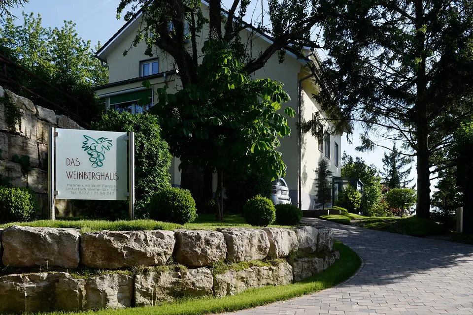 Einfahrt zum Weinberghaus Fellbach mit Namensschild, Natursteinmauer und gepflasterter Zufahrt zwischen Bäumen