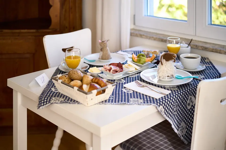 Gedeckter Frühstückstisch im Weinberghaus: Brötchenkorb, Orangensaft, Kaffee, Wurst, Käse und Obst am Fenster