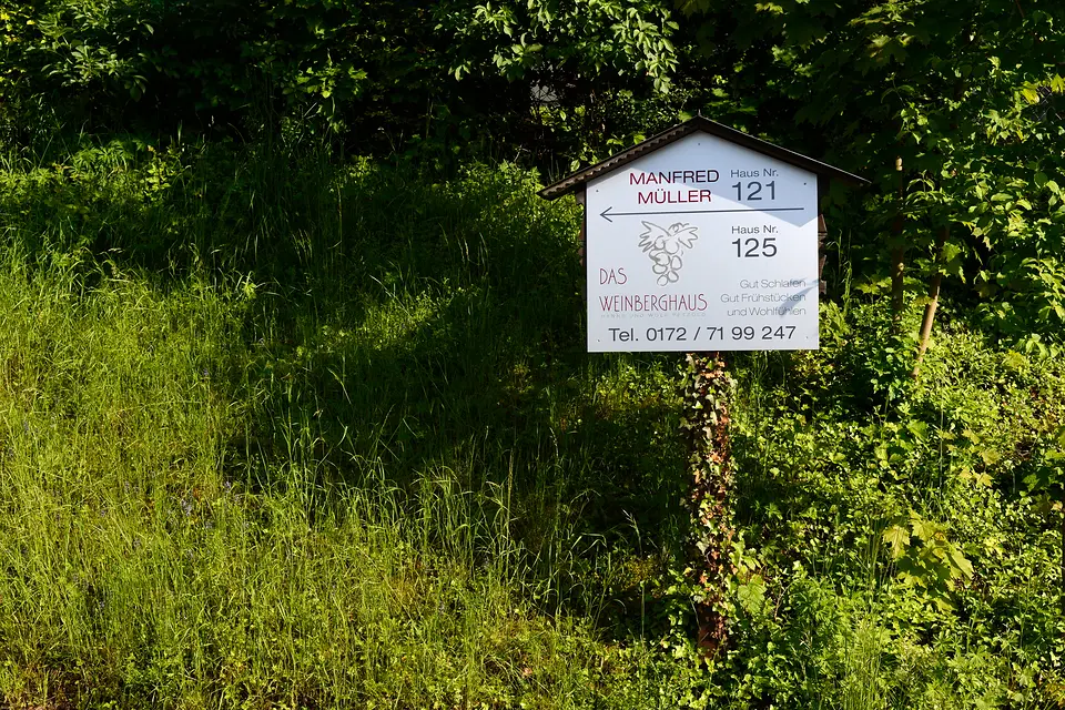 Wegweiser am Wegrand zwischen Hecken und Wiese: Das Weinberghaus, Haus Nr. 125