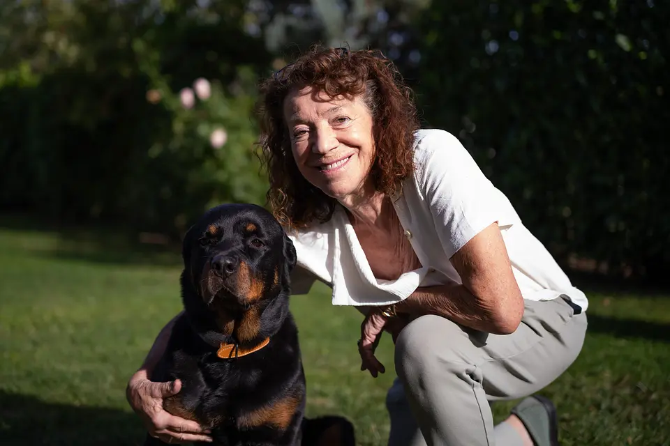Hanne Petzold kniet lächelnd neben dem Rottweiler der Familie im Garten