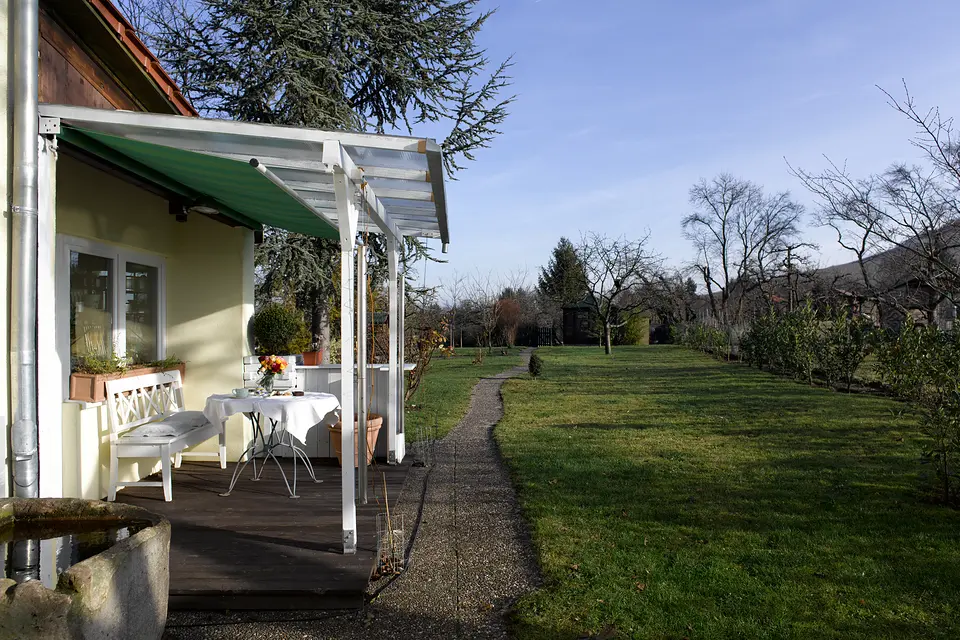 Terrasse mit Markise und kleinem Tisch, davor der lange Rasenweg durch den Garten des Weinberghauses