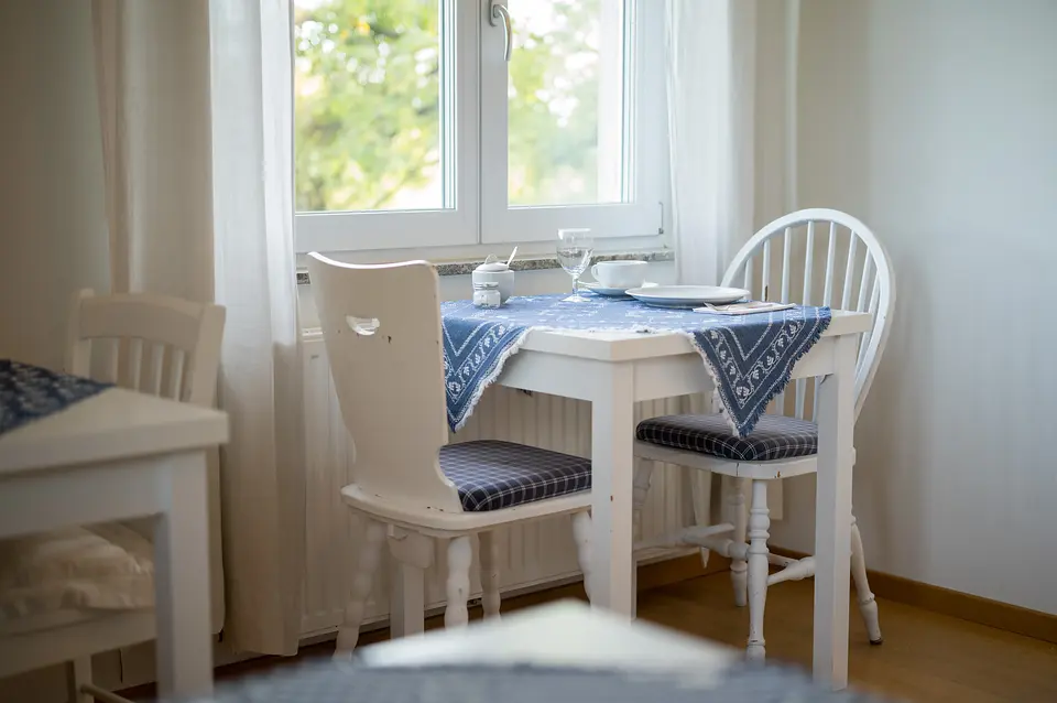 Kleiner Frühstückstisch für zwei am Fenster mit blau-weißer Tischdecke und Blick in den Garten