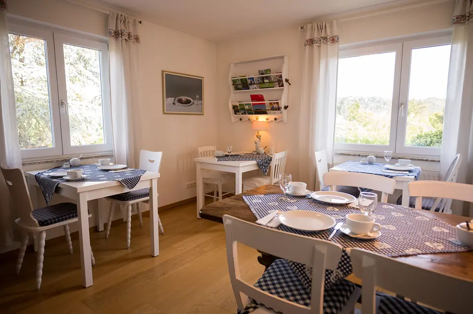 Das Frühstückszimmer im Weinberghaus: weiße Tische mit blau gemusterten Decken und zwei helle Fenster zum Garten