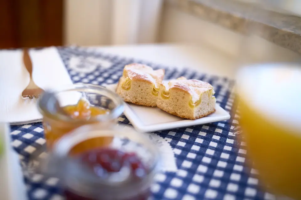 Marmelade im Glas und Hefeteilchen auf dem Frühstückstisch, daneben ein Glas Orangensaft