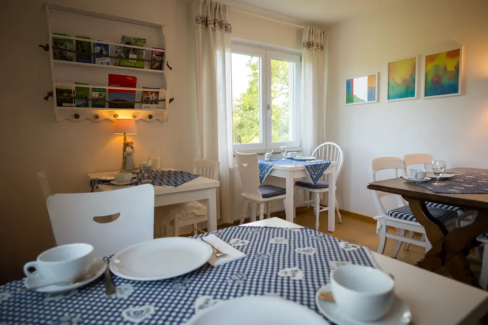 Frühstückszimmer mit gedeckten Tischen, Prospektregal an der Wand und Blick aus dem Fenster ins Grüne