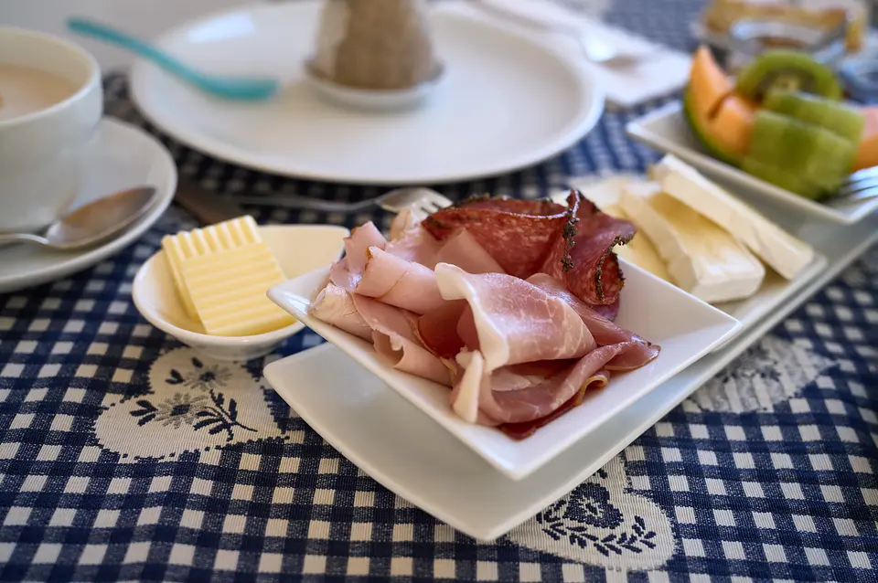 Teller mit Schinken und Salami, dazu Butter, Käse, Melone und Kiwi auf blau-weißer Tischdecke