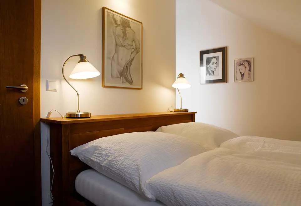 Schlafnische im Grünen Zimmer: Doppelbett mit Holzkopfteil, zwei Nachttischlampen und Zeichnungen an der Wand