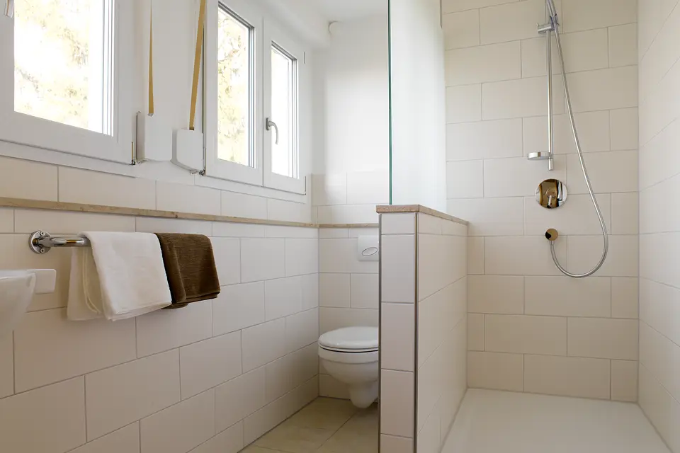 Badezimmer des Grünen Zimmers: weiße Fliesen, ebenerdige Dusche, Fenster und frische Handtücher