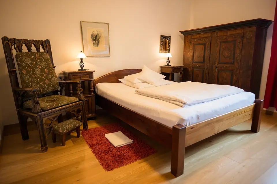 Bauernzimmer mit Holzbett, geschnitztem Lehnstuhl, Nachttischlampen und rotem Teppich auf Parkett