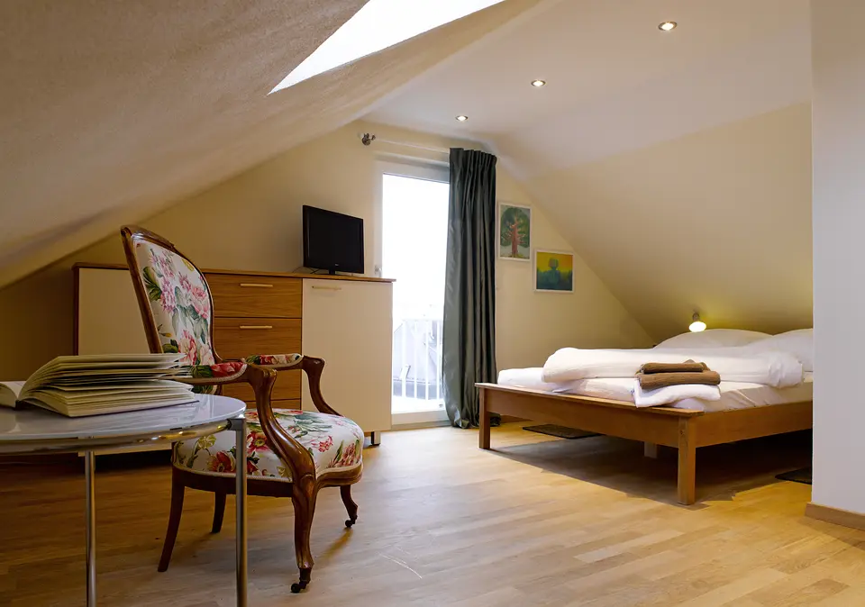 Stuttgarter Zimmer unter dem Dach: Holzbett, geblümter Sessel, Kommode mit Fernseher und Balkontür
