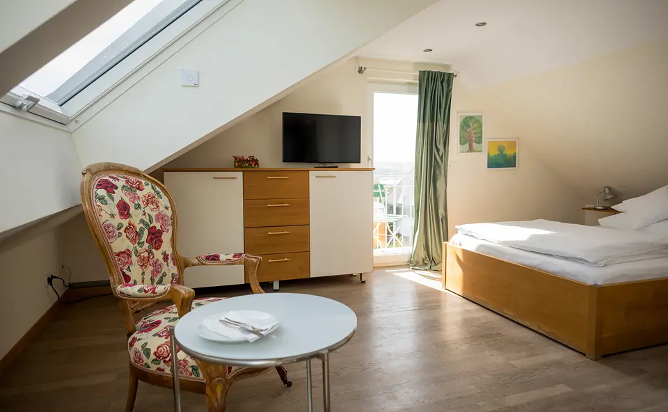 Stuttgarter Zimmer mit Dachfenster, geblümtem Sessel, Tischchen, Kommode mit Fernseher, Doppelbett und Balkontür