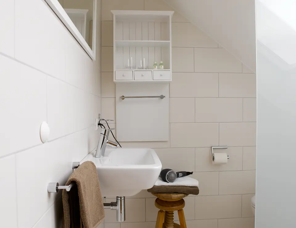 Badezimmer des Stuttgarter Zimmers mit Waschbecken, weißem Wandregal, Handtüchern und Föhn unter der Dachschräge