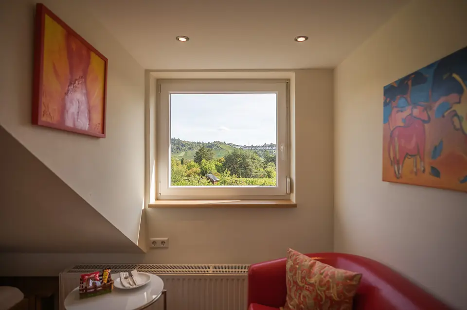 Weinberg-Zimmer: Fenster mit Blick auf die Weinberge, rote Ledercouch und zwei farbenfrohe Bilder